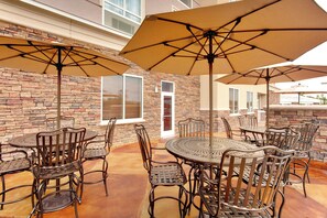 Un espace extérieur aménagé en terrasse, avec plusieurs tables et chaises rondes, protégé par de grands parasols, le tout adossé à un mur en pierre.