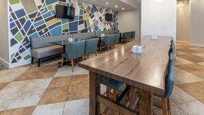 Un comedor moderno con una larga mesa de madera, asientos acolchados y un llamativo diseño abstracto en la pared.