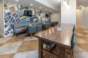 Un comedor moderno con una larga mesa de madera, asientos acolchados y un llamativo diseño abstracto en la pared.
