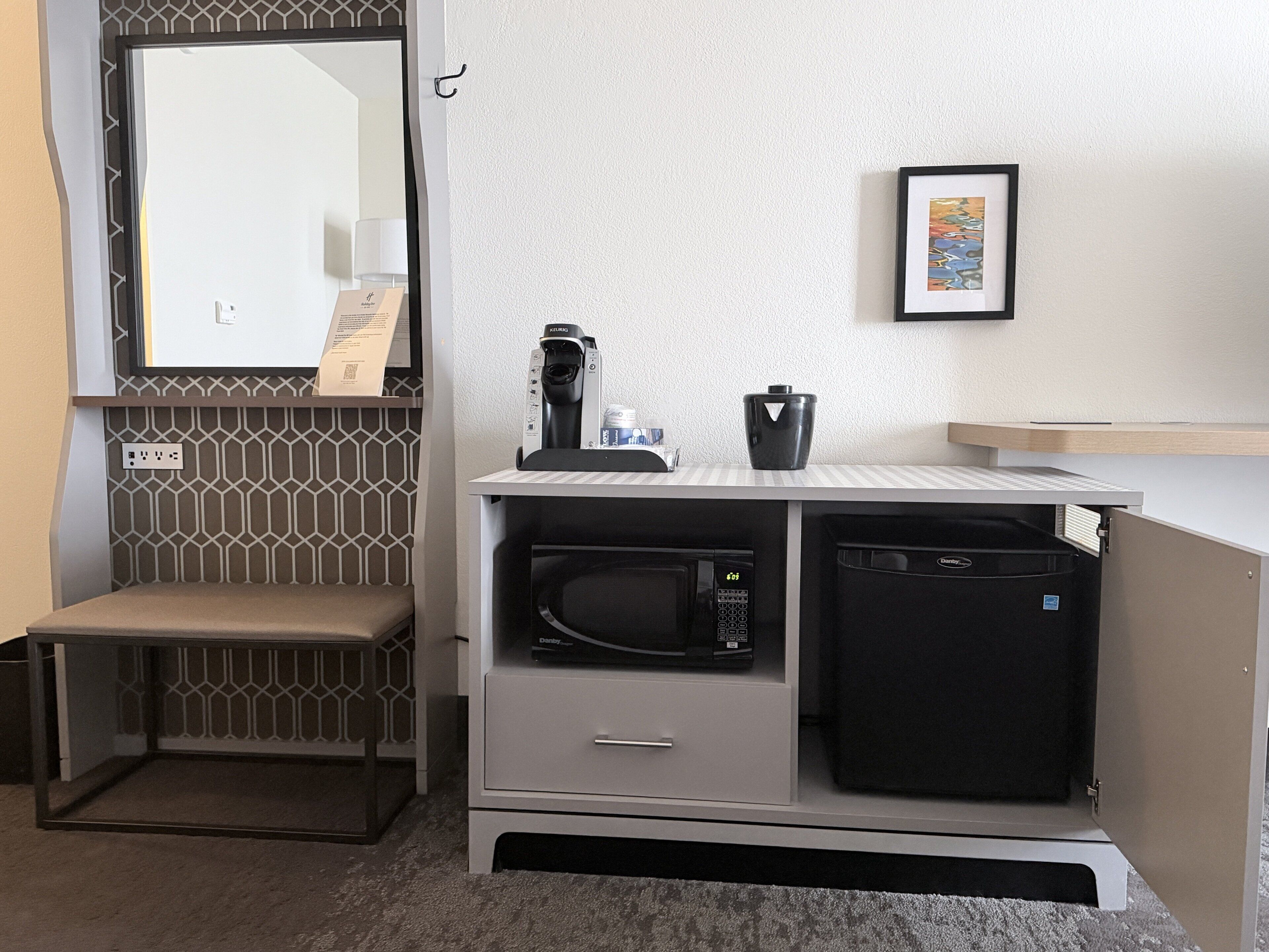 Een kleine kitchenette met een magnetron, koffiezetapparaat en een kastje.
