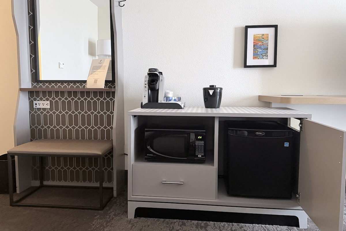Een kleine kitchenette met een magnetron, koffiezetapparaat en een kastje.
