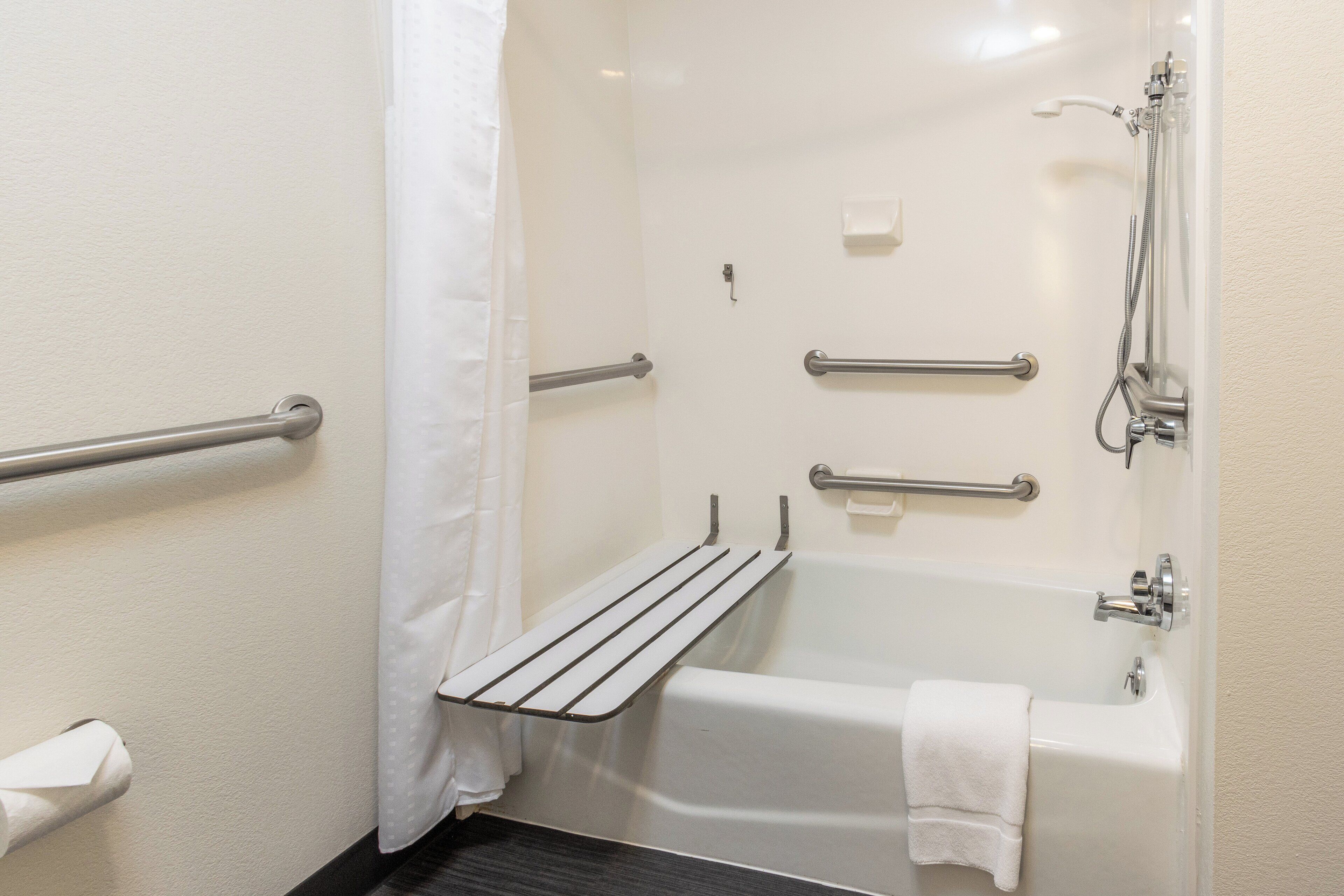 A bathroom with a bathtub, grab bars, a towel rack, and a shower head.
