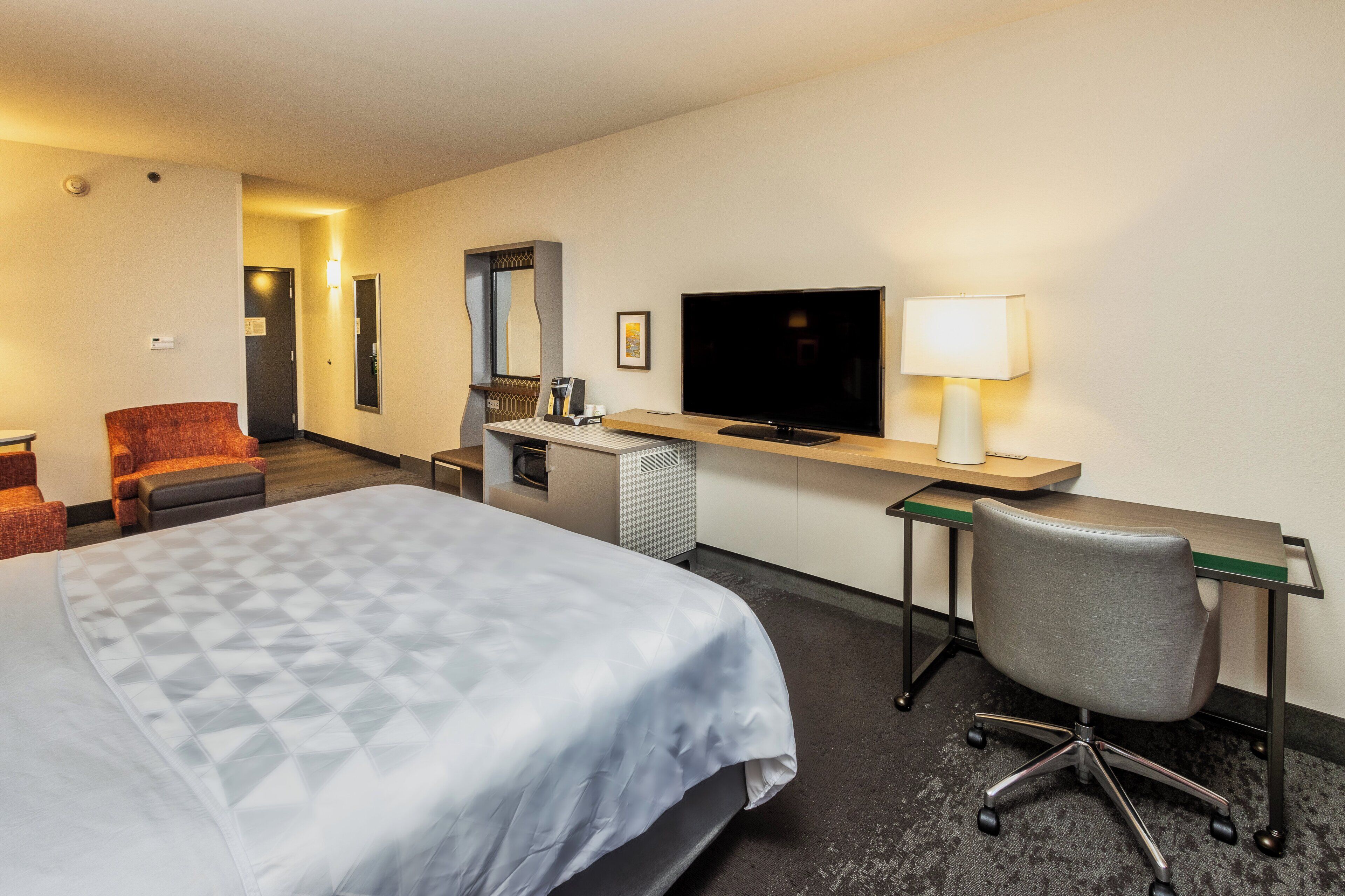 A hotel room with a bed, desk, chair, television, and a small kitchenette.