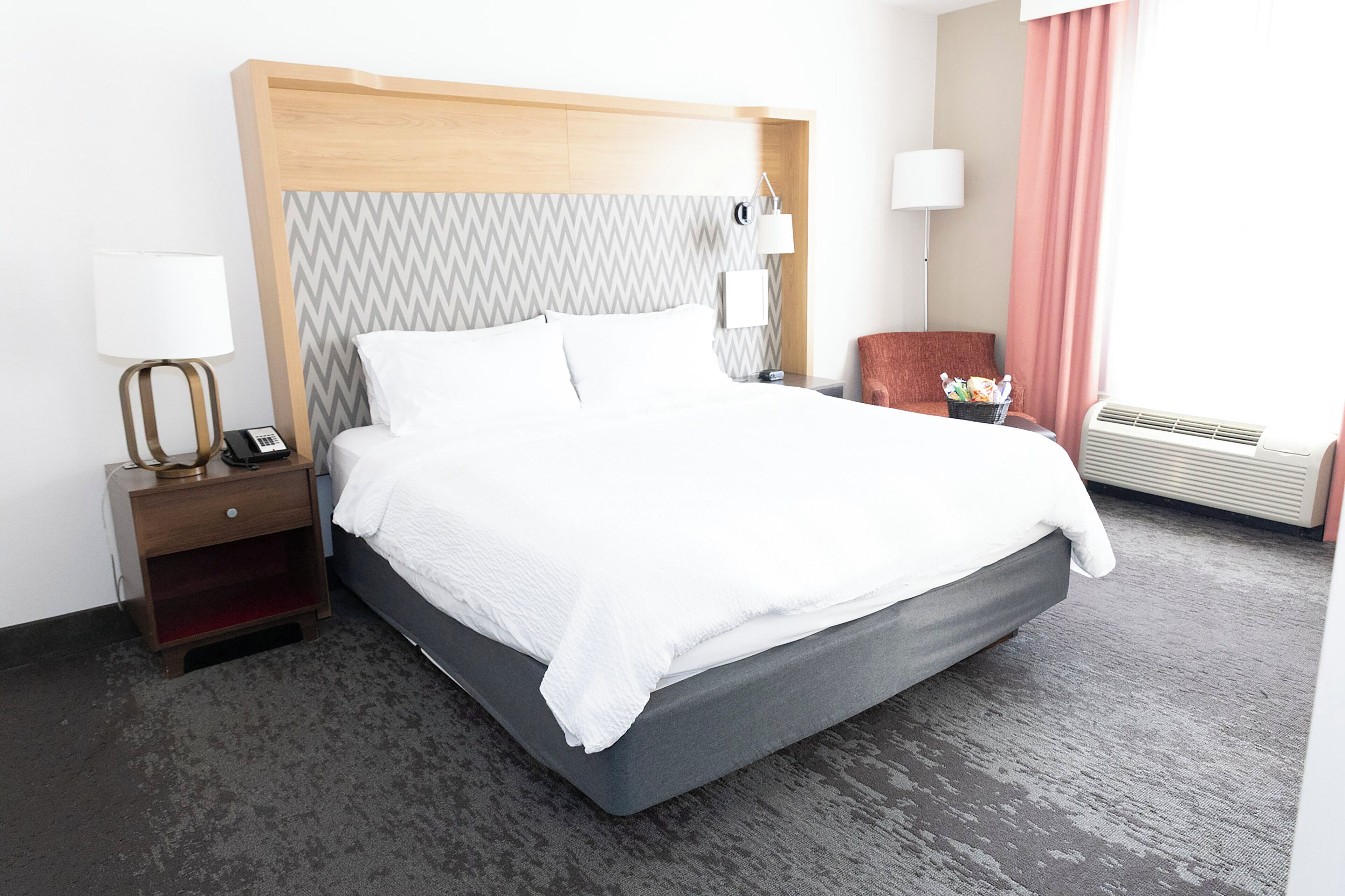A neatly made bed with white linens, a wooden headboard, a nightstand with a lamp, and a chair.