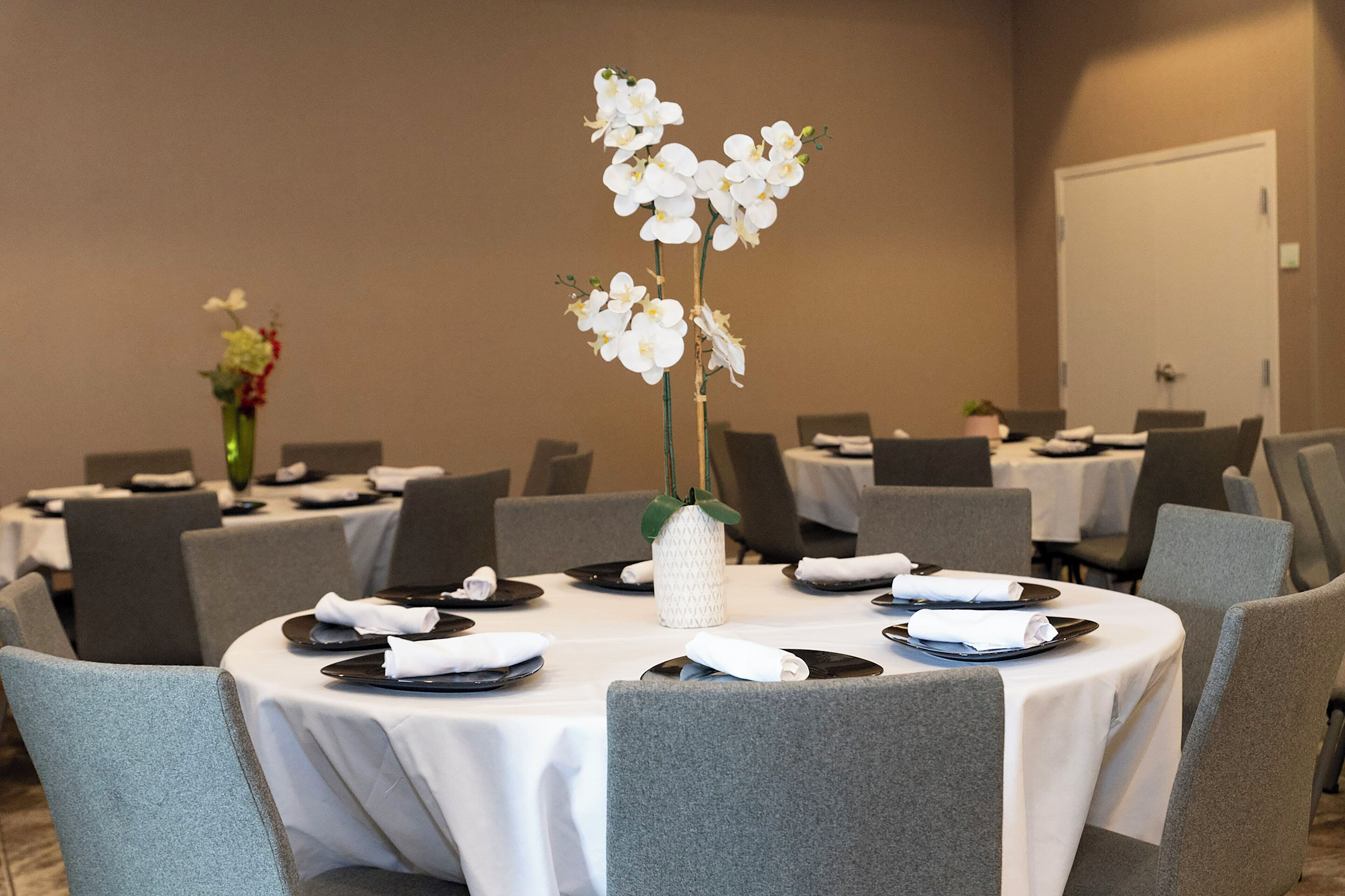 A conference room with round tables, grey chairs, and white tablecloths.