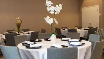 A conference room with round tables, grey chairs, and white tablecloths.