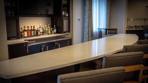 Una zona de bar con una barra larga, varias sillas y una variedad de botellas en estanterías.