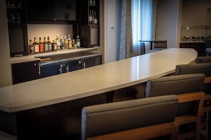 Un espace bar avec un long comptoir, plusieurs chaises et une variété de bouteilles exposées sur des étagères.