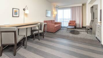 A hotel room with a desk, two chairs, a sofa, a small table, and a television.