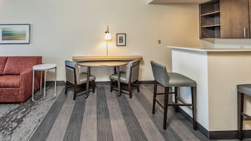 A compact hotel room with a dining area, a sofa, and a small bar counter.