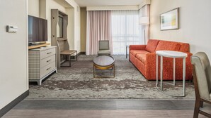 Una habitación de hotel con sofá, una mesita redonda, televisor, cómoda y una silla.