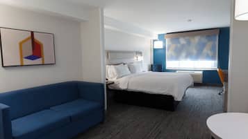 A hotel room with a bed, a blue sofa, a painting on the wall, and a window with blinds.