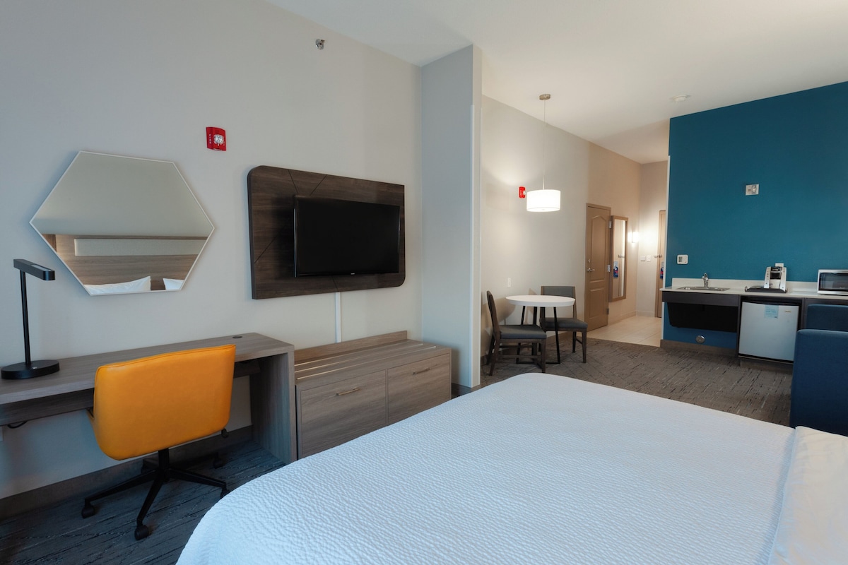 A hotel room with a bed, desk, chair, television, and a small dining area.