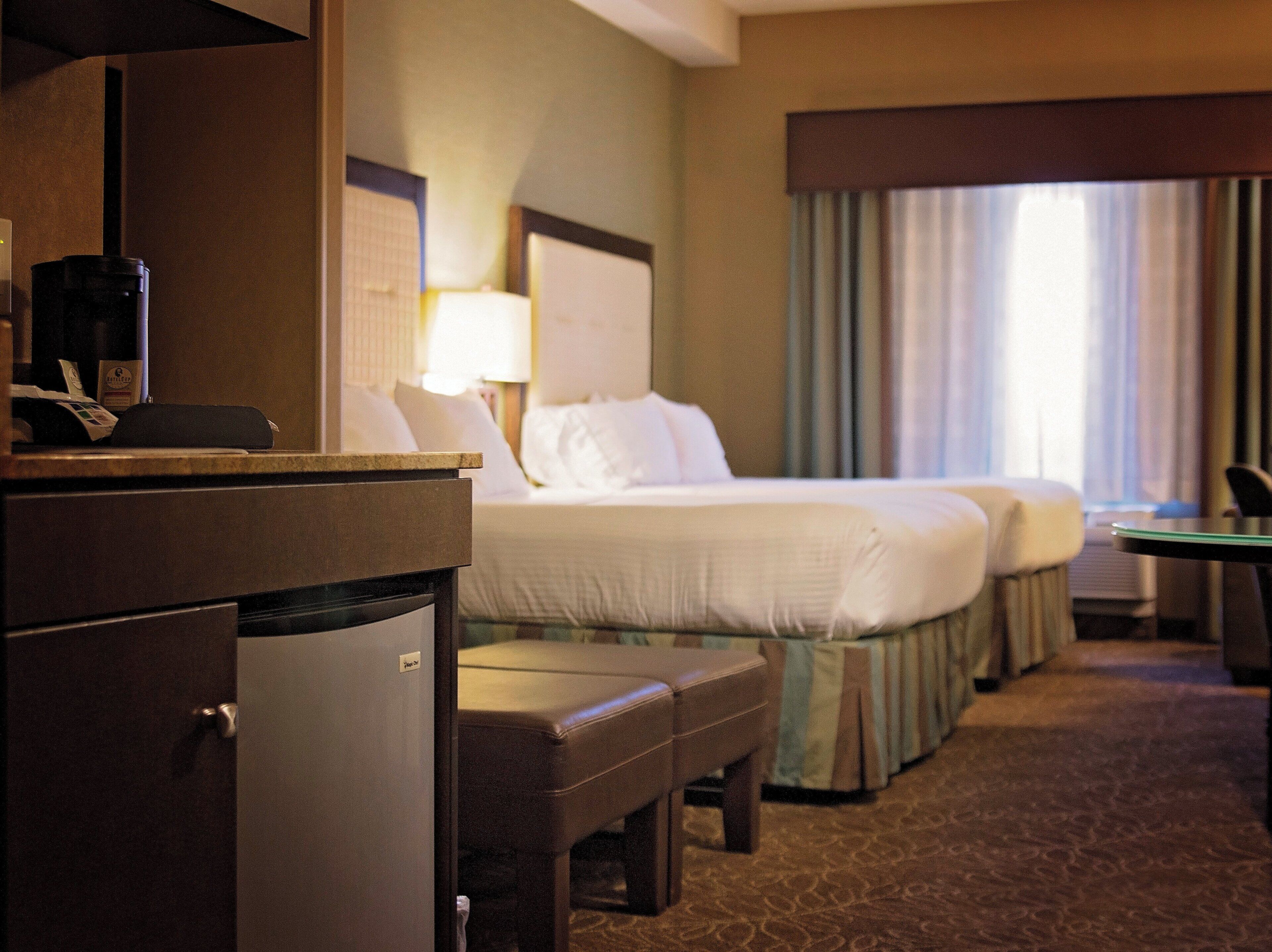 A hotel room with a bed, a desk, a chair, a small table, and a minibar.