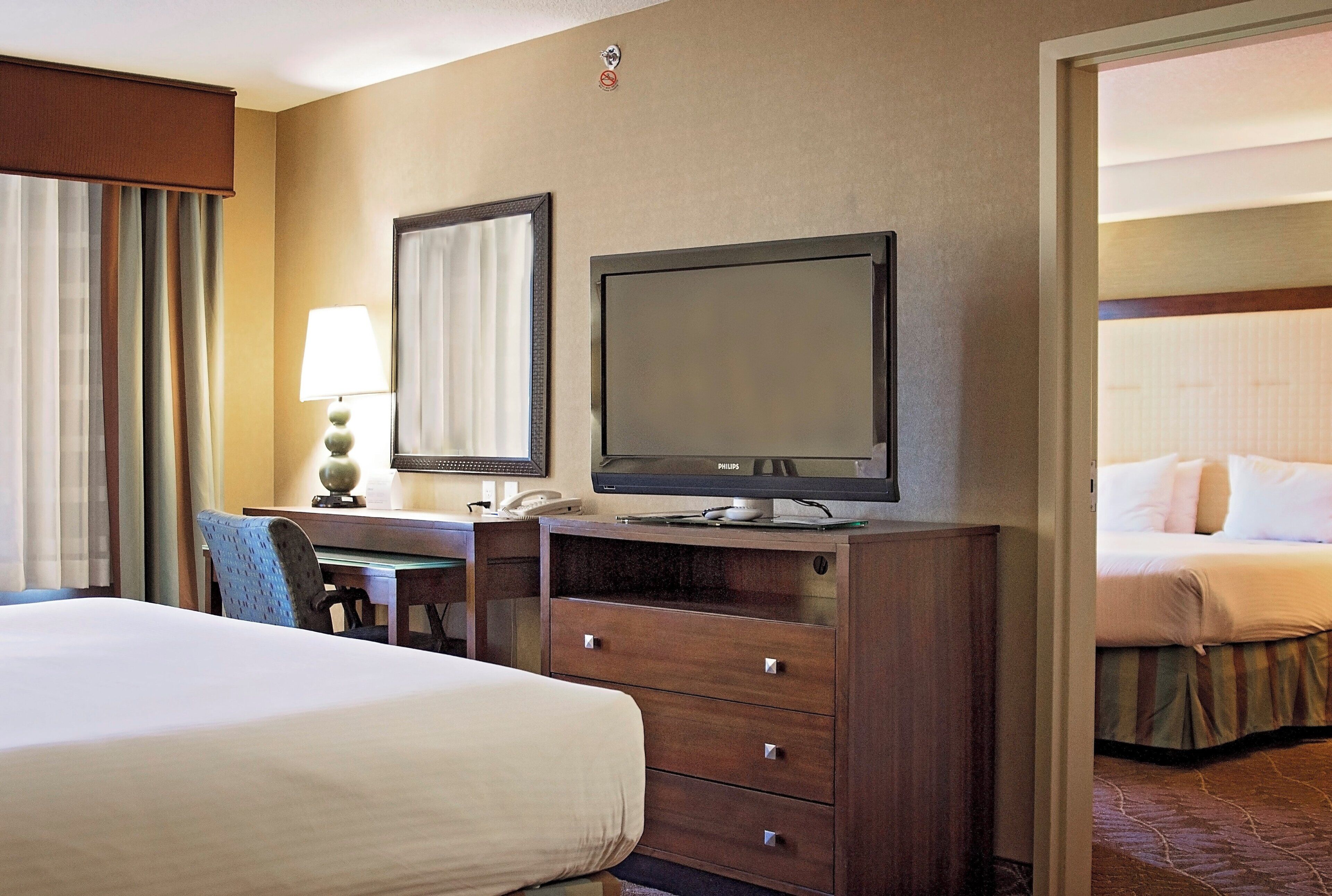 A hotel room with a bed, a desk with a lamp, a television, and a mirror.