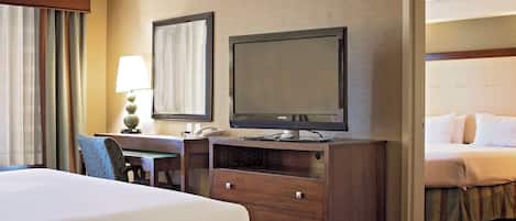 Una habitación de hotel con una cama, un escritorio con una lámpara, un televisor y un espejo.