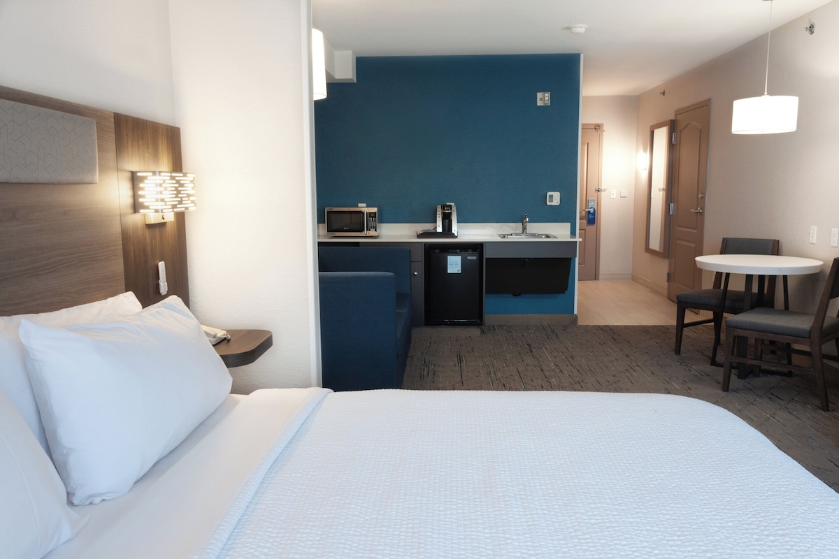 A hotel room with a bed, a desk, a microwave, a coffee maker, and a small table with chairs.
