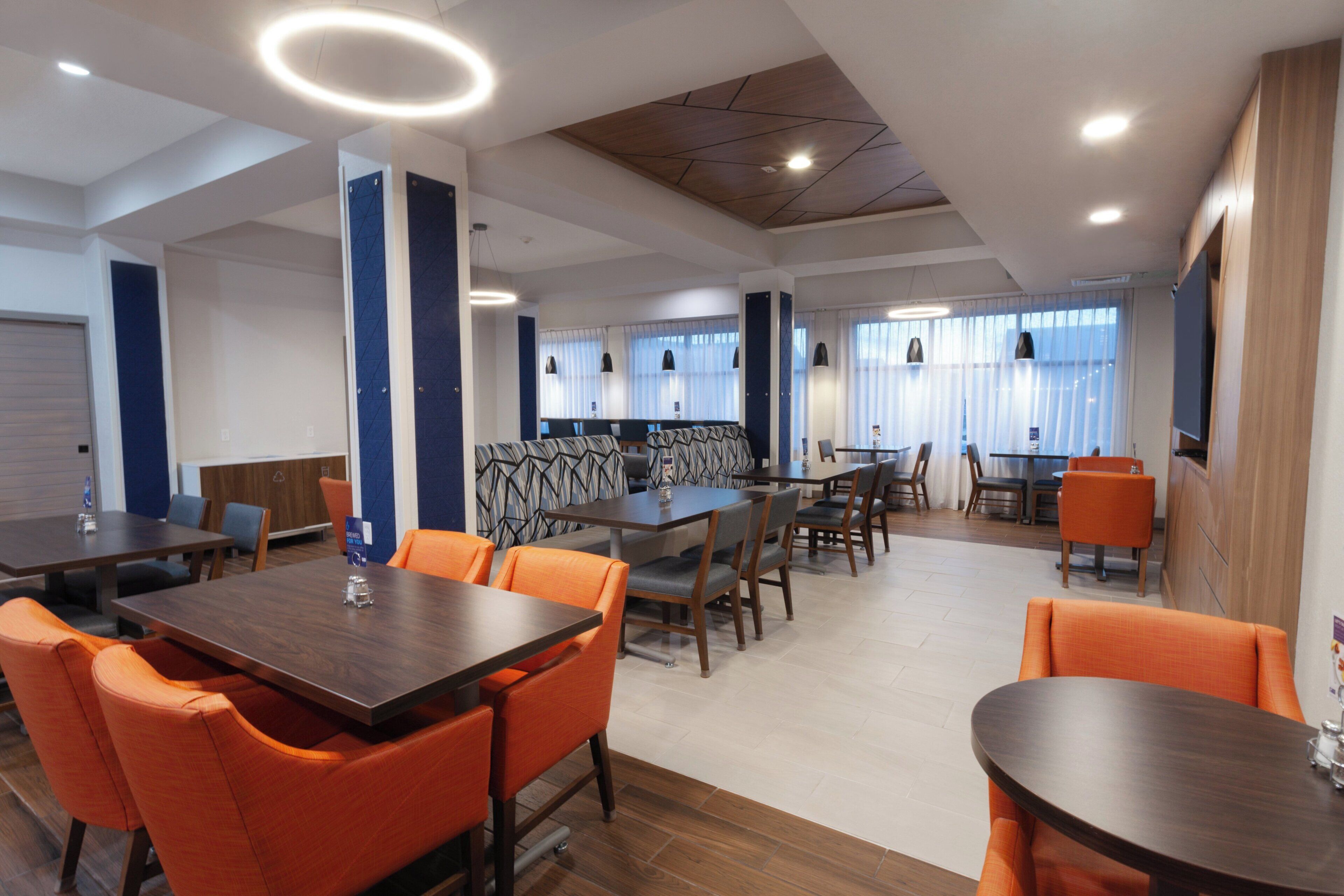 A modern dining area with multiple tables and chairs, a patterned wall, and pendant lighting.