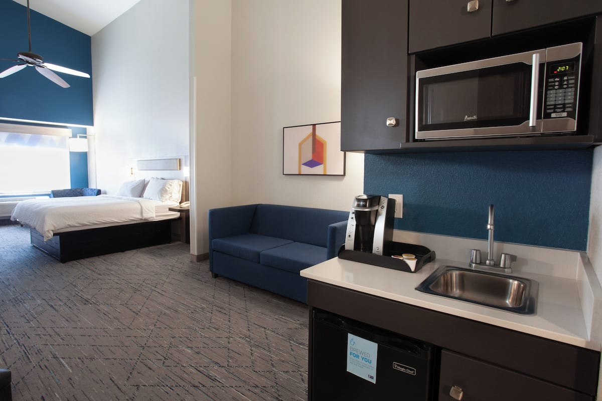 A hotel room with a bed, a sofa, a kitchenette with a microwave, a coffee maker, and a sink.