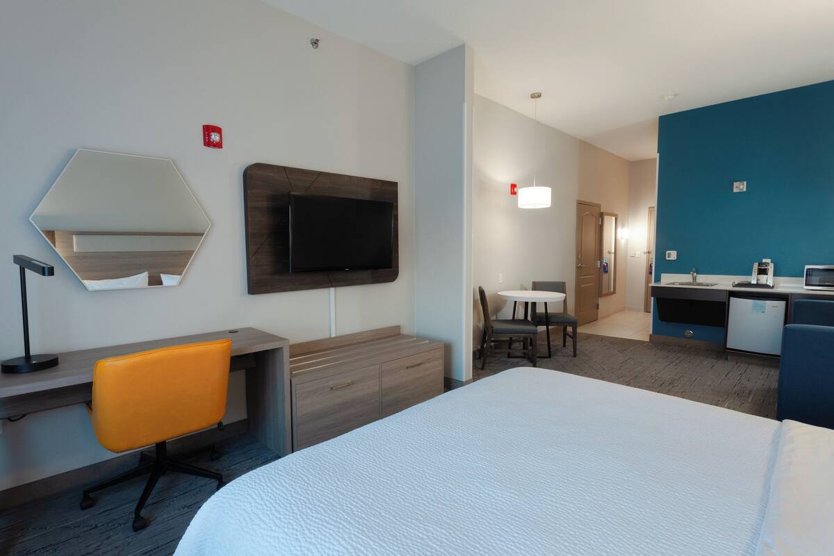 A hotel room with a bed, desk, chair, television, and a small dining area.