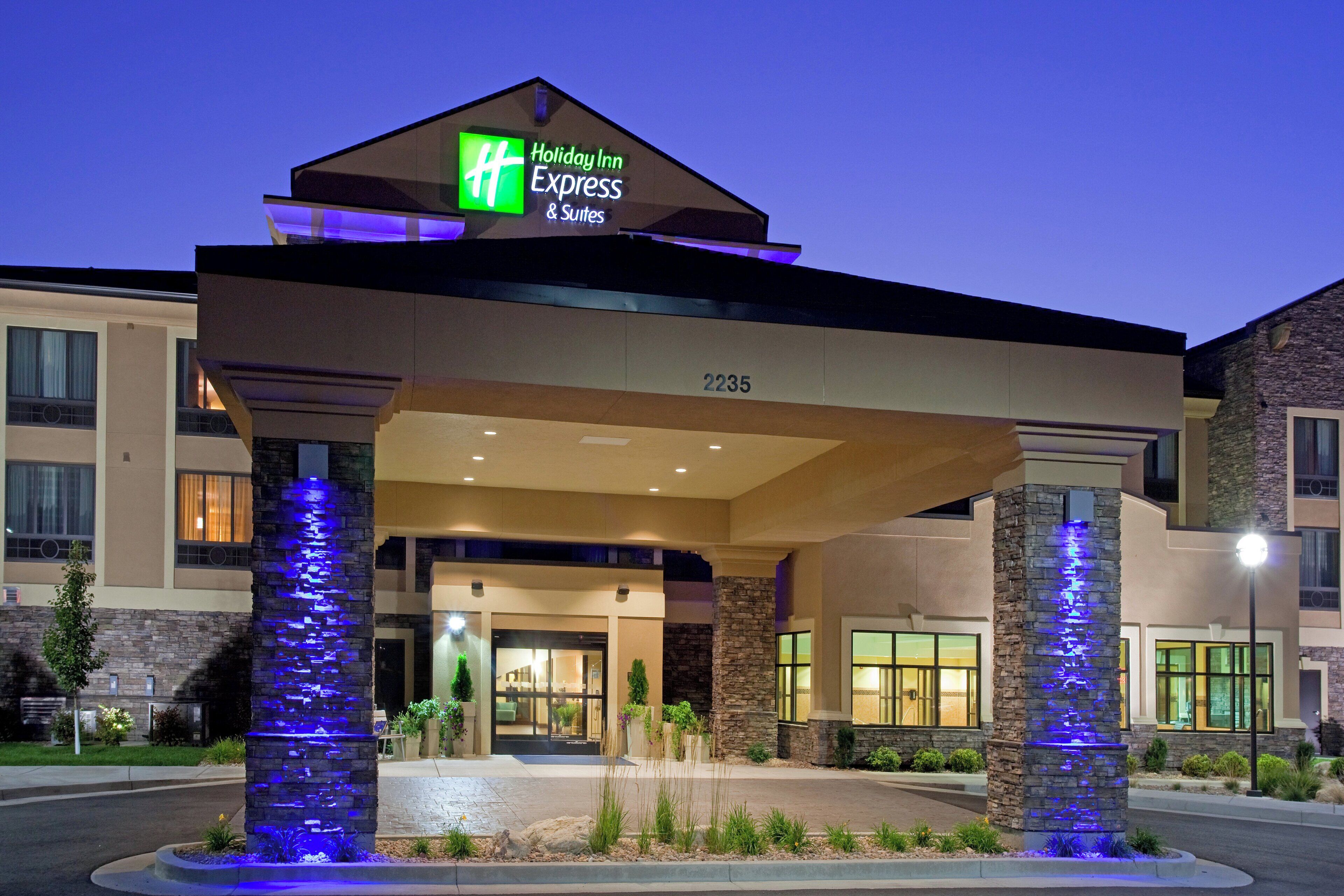 A Holiday Inn Express & Suites building with a modern design, featuring a prominent entrance and illuminated pillars.
