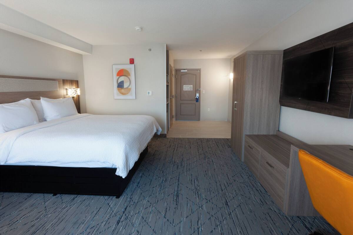 A hotel room with a bed, a TV, a desk, and a door leading to a hallway.