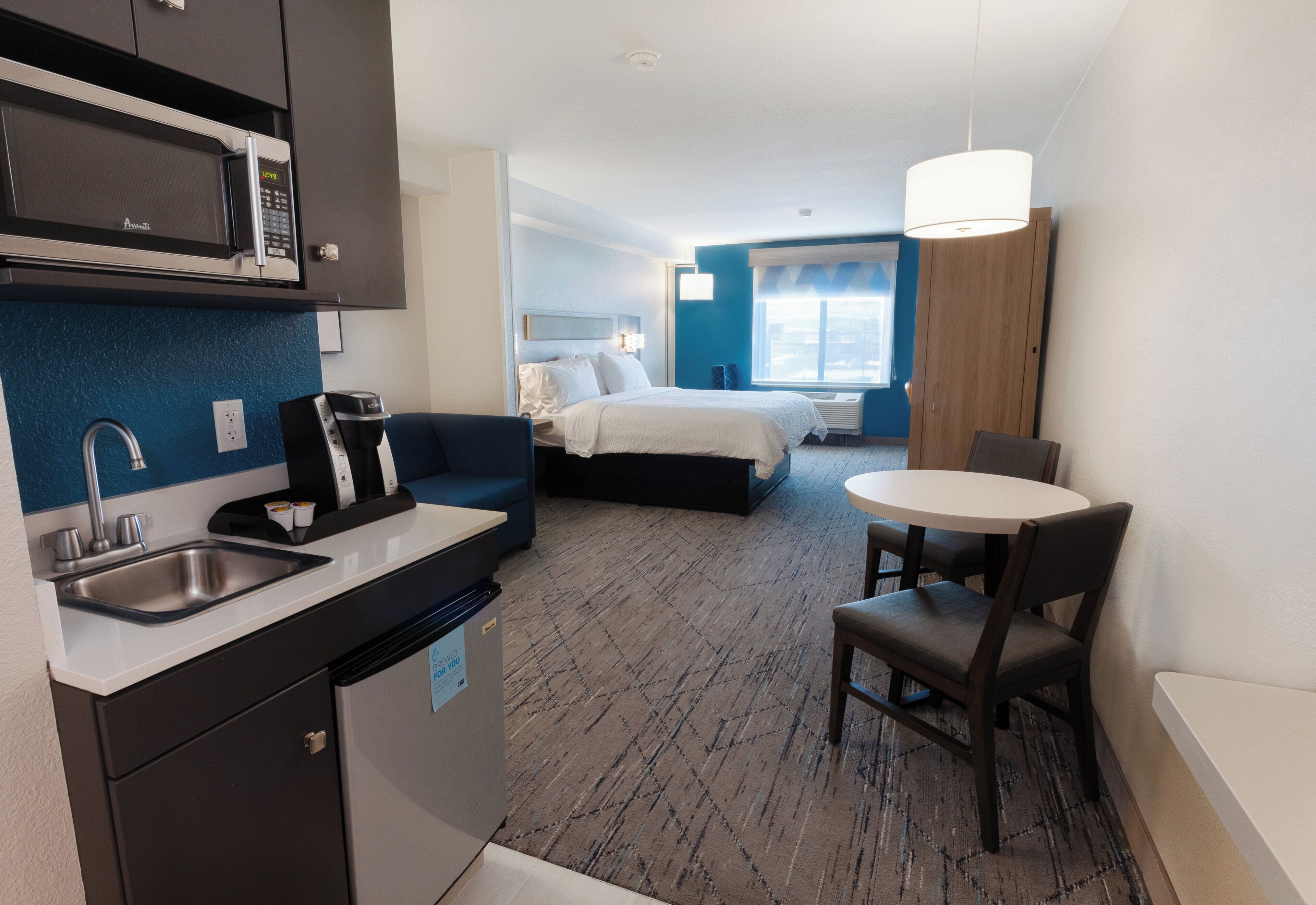 Una habitación de hotel con kitchenette, una cama, zona de comedor y un ventanal grande.