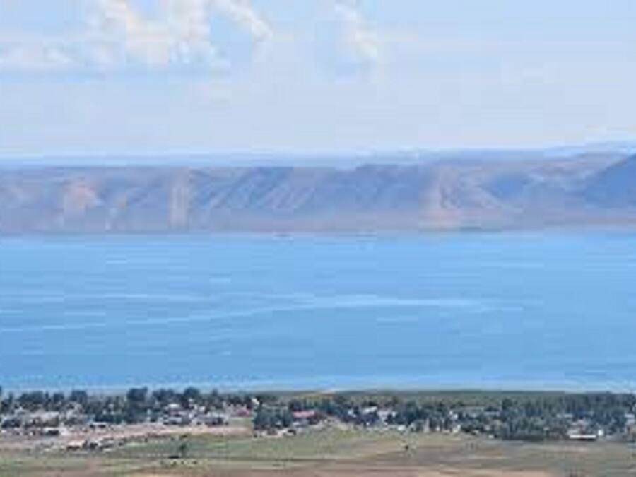 A coastal landscape with a body of water, a distant mountain range, and a small settlement with buildings and greenery at the shore.