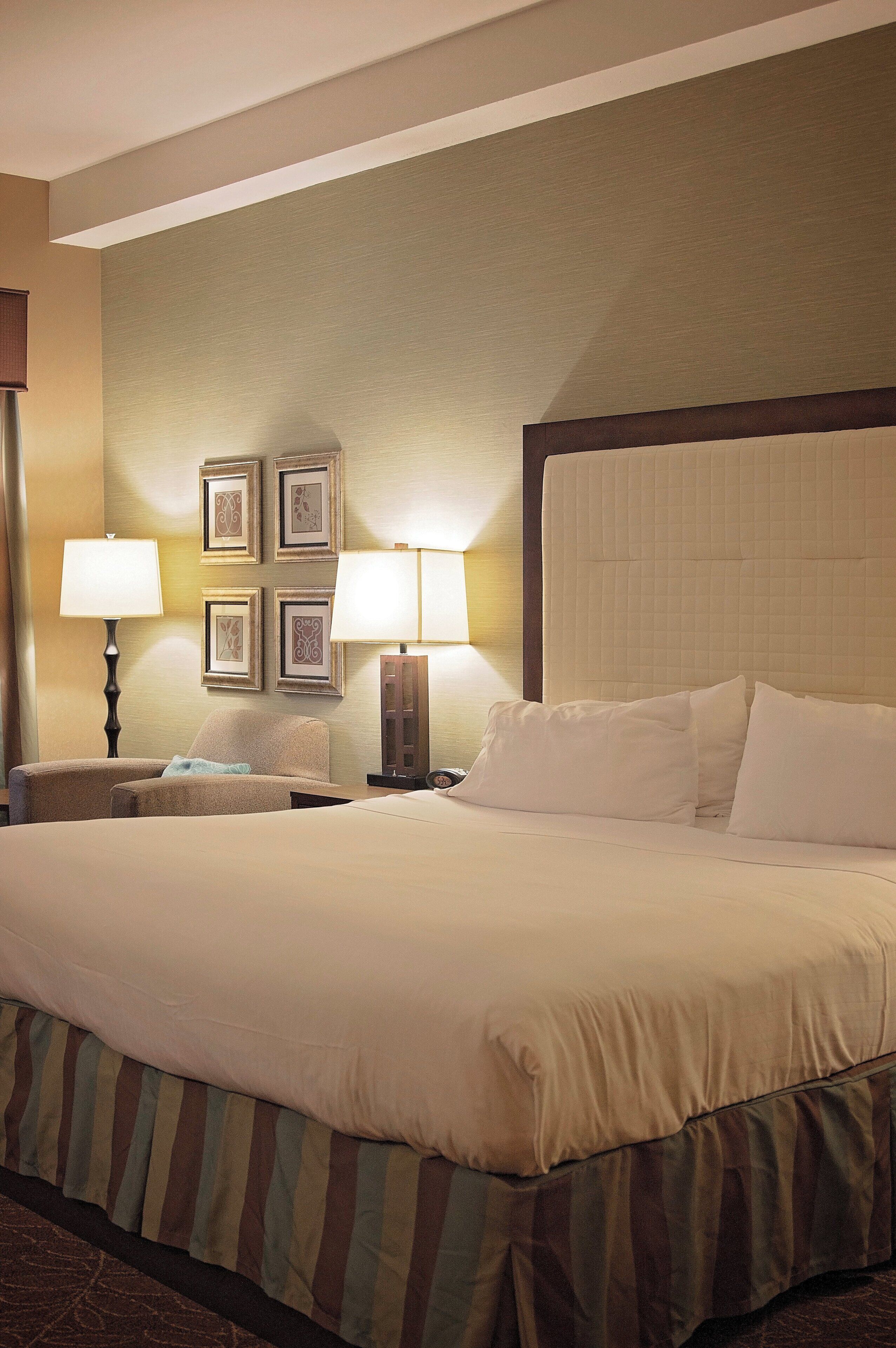 A hotel room with a large bed, two bedside lamps, a headboard, and framed pictures on the wall.