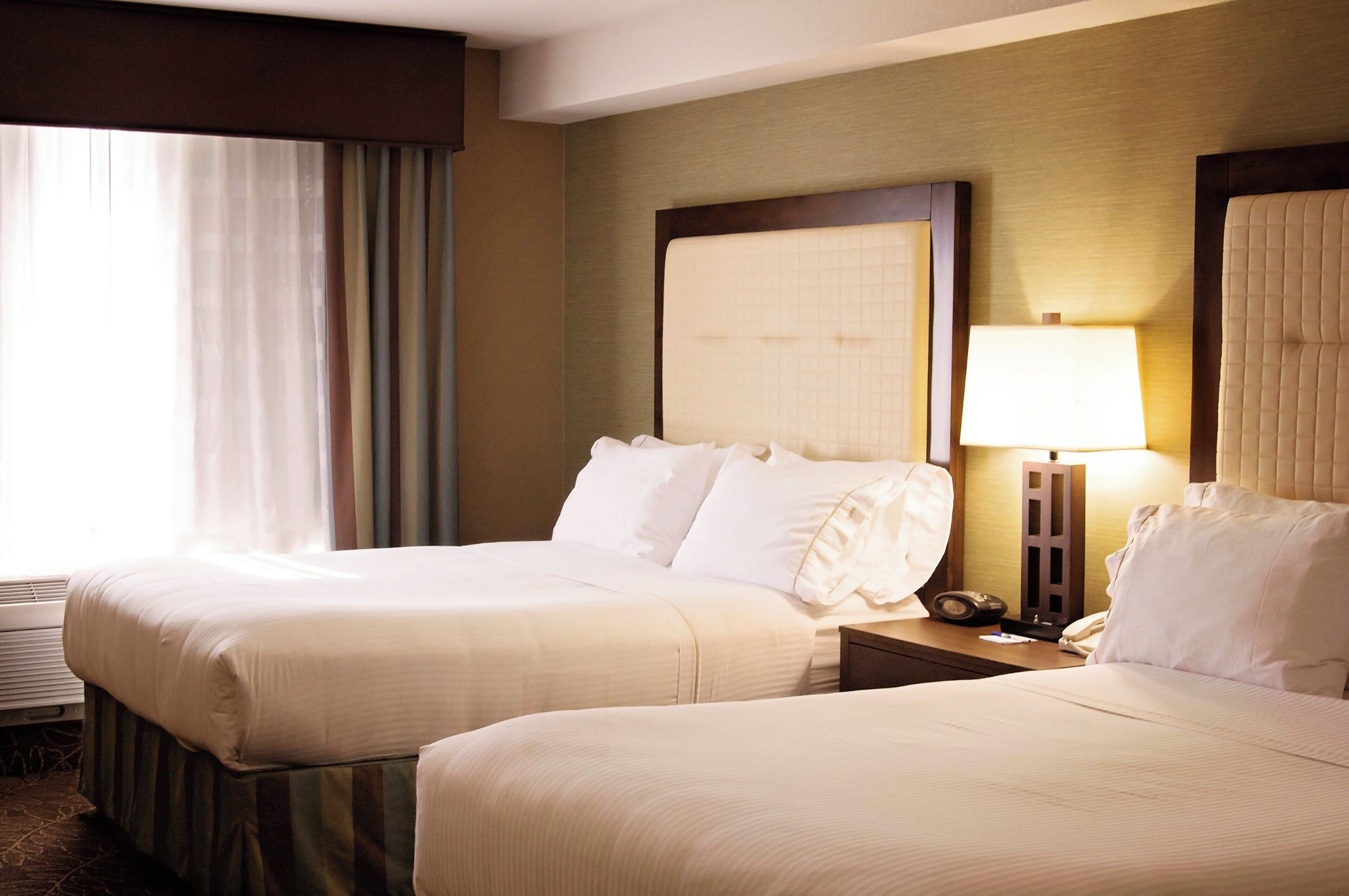 A hotel room with two beds, a nightstand with a lamp, and a window with curtains.