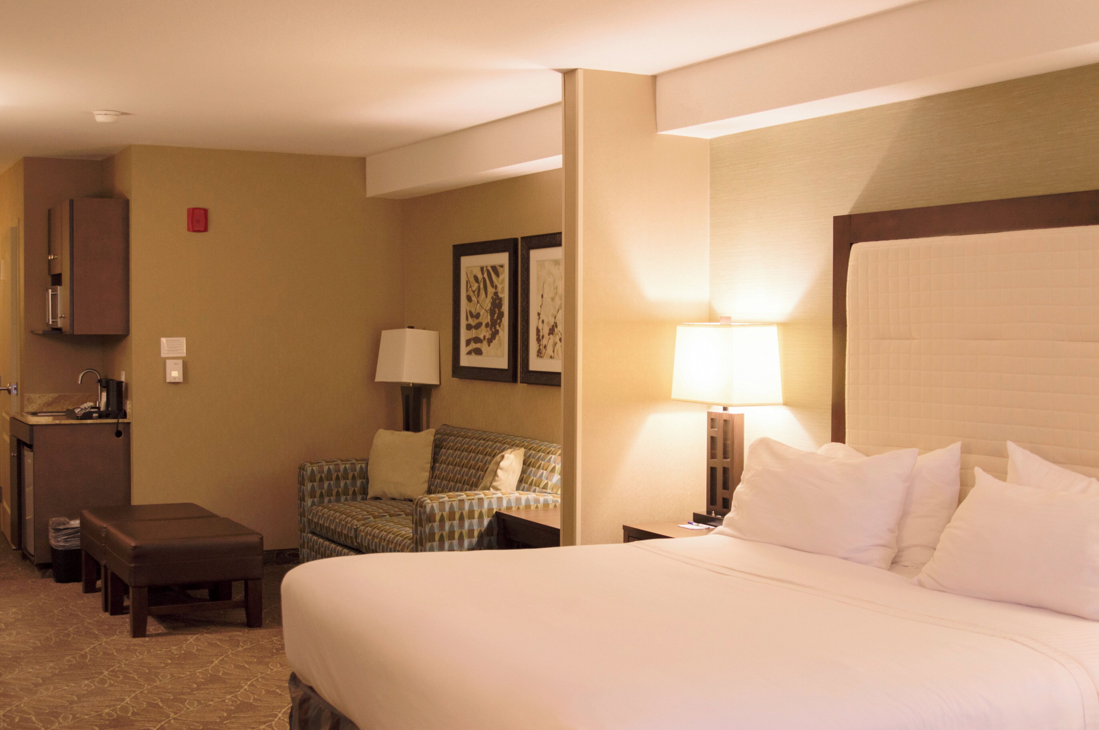 A hotel room with a bed, a desk, a chair, a small table, a nightstand, a lamp, a picture frame, and a cabinet.