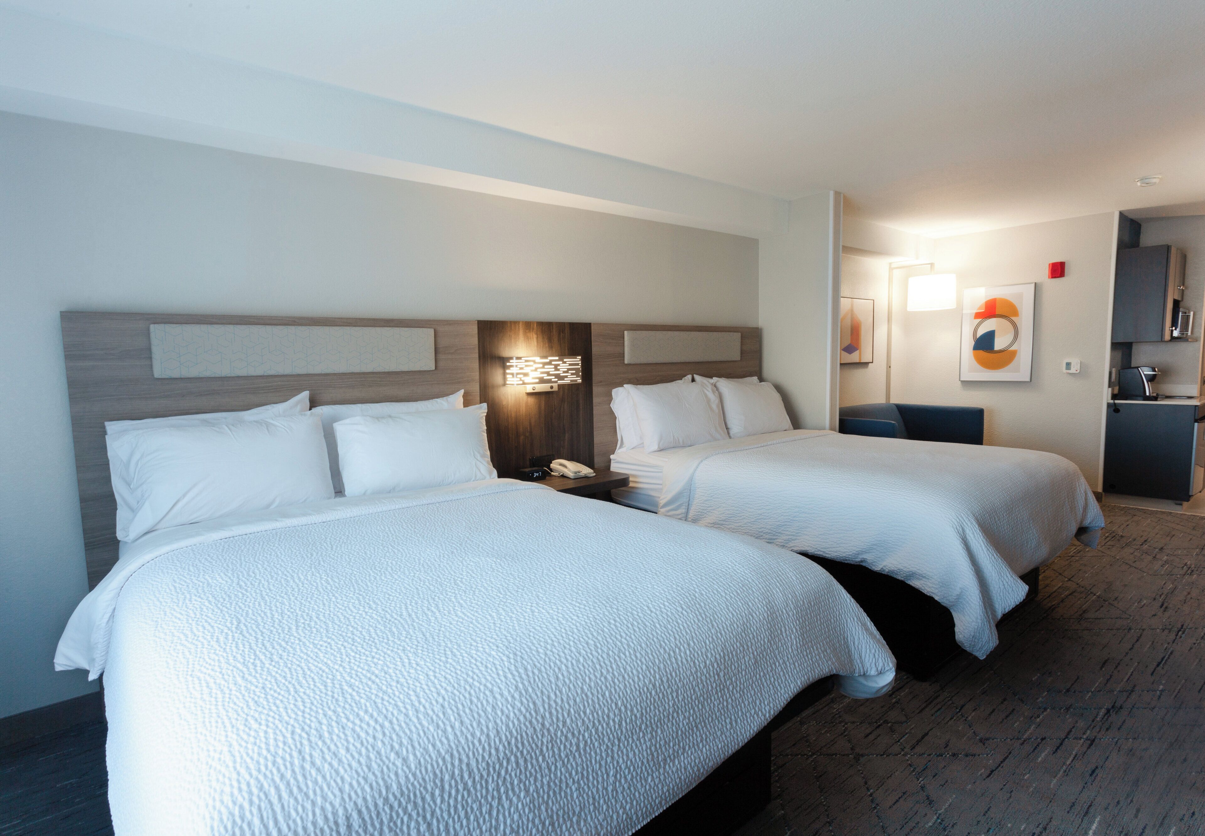 Ein Hotelzimmer mit zwei Betten, einem Nachttisch, einer Wandlampe und einem kleinen Schreibtisch mit Stuhl.