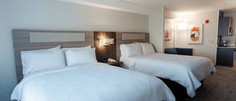 A hotel room with two beds, a nightstand, a wall-mounted lamp, and a small desk with a chair.