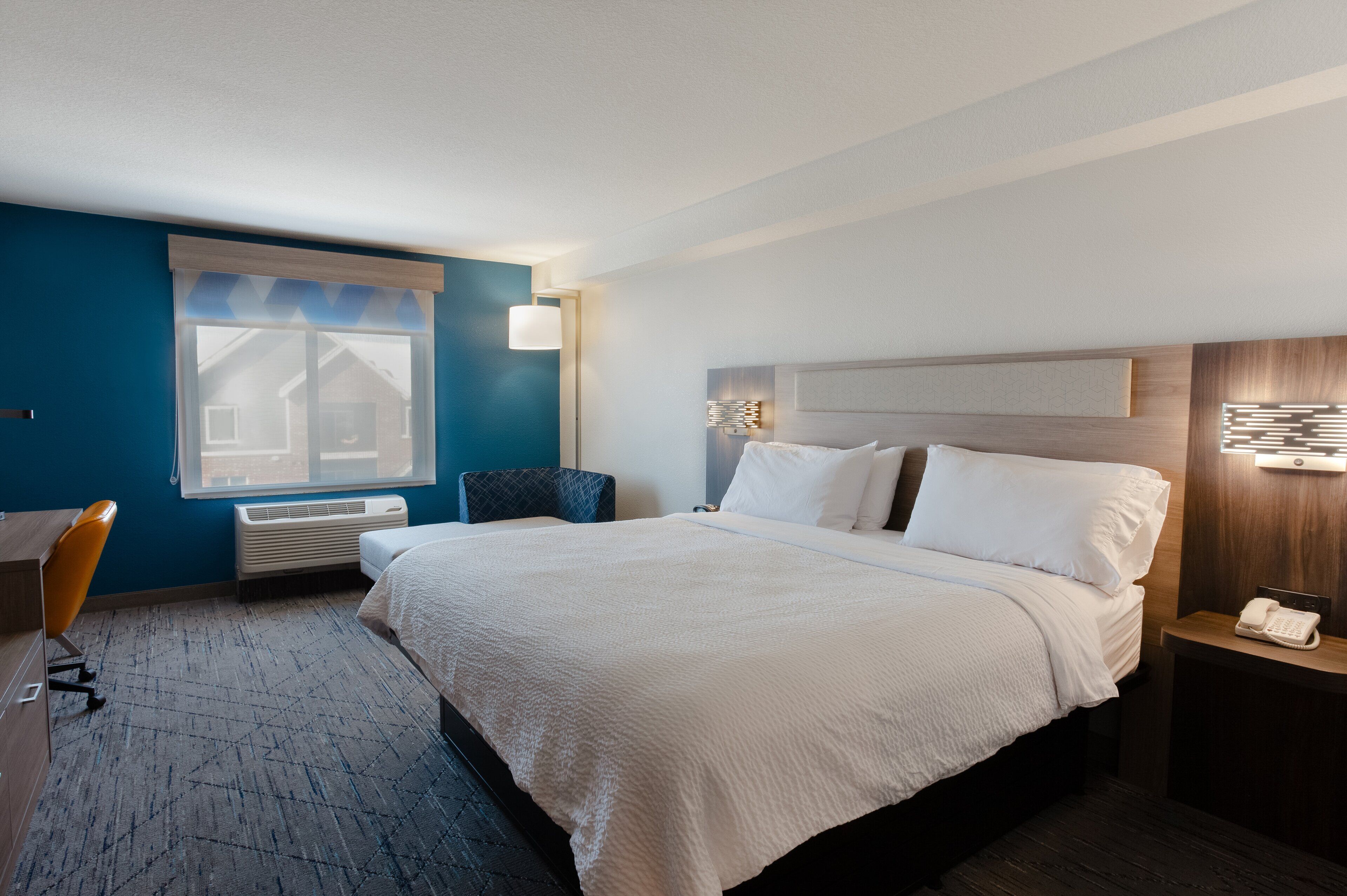 Een hotelkamer met een groot bed, een bureau, een stoel, een raam en een nachtkastje met een telefoon.