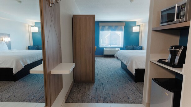 Hotellihuone, jossa on kaksi sänkyä, mikroaaltouuni, kahvinkeitin, minijääkaappi, työpöytä ja ikkuna, jossa on verhot.