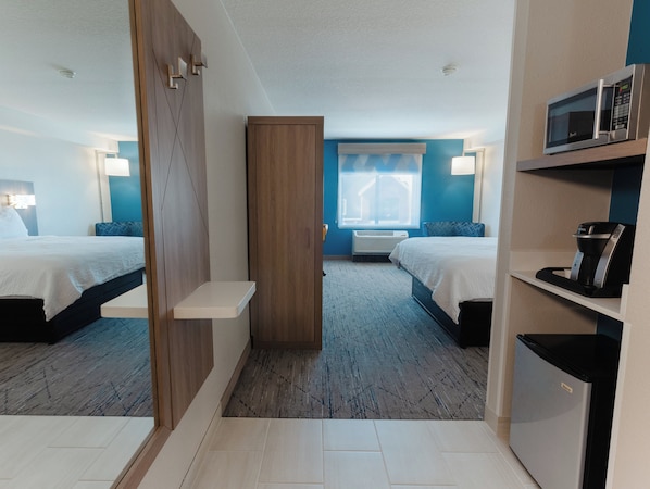 A hotel room with two beds, a microwave, a coffee machine, a mini-fridge, a desk, and a window with curtains.