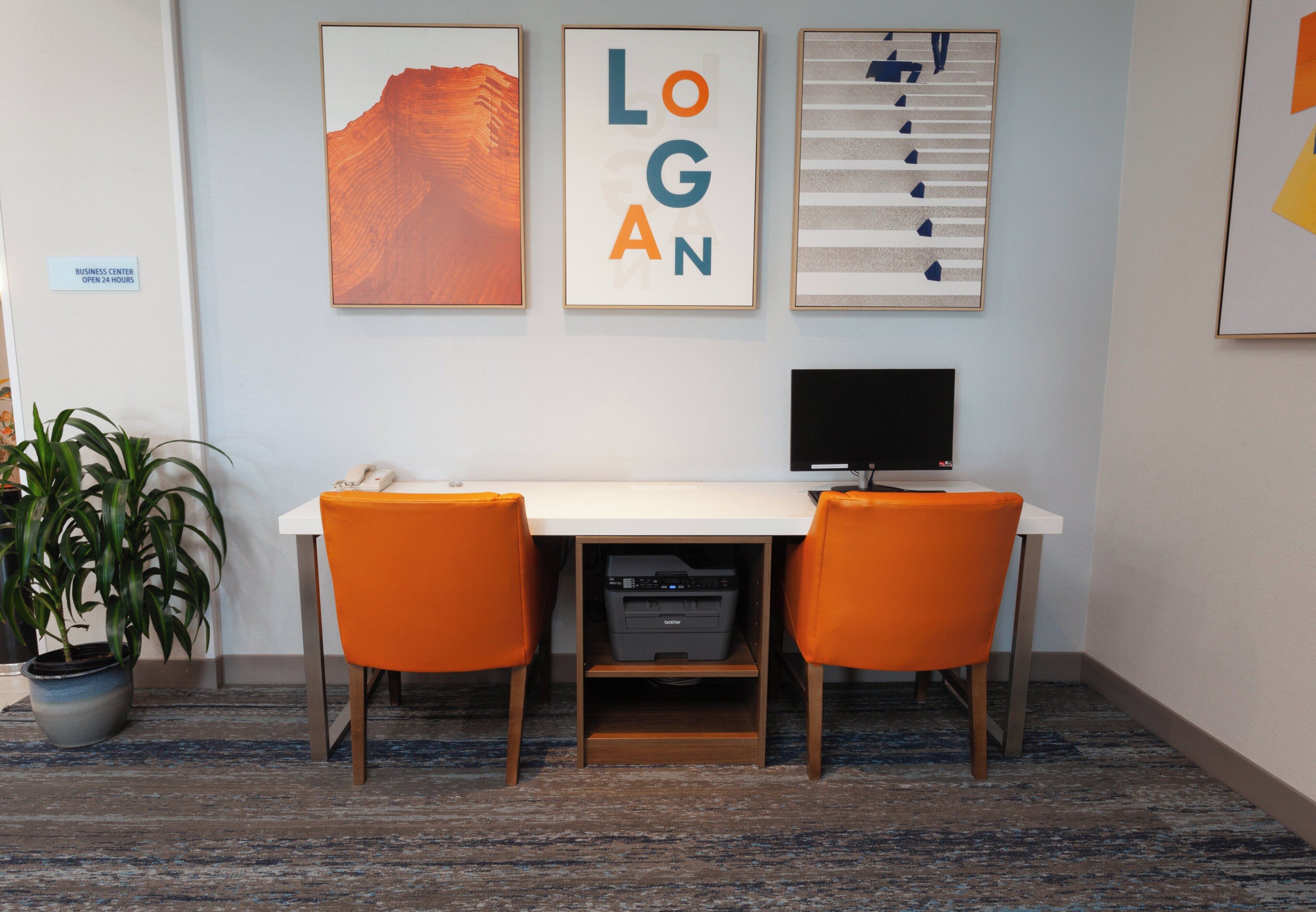 A business center with a desk, two orange chairs, a printer, and framed artwork on the wall.
