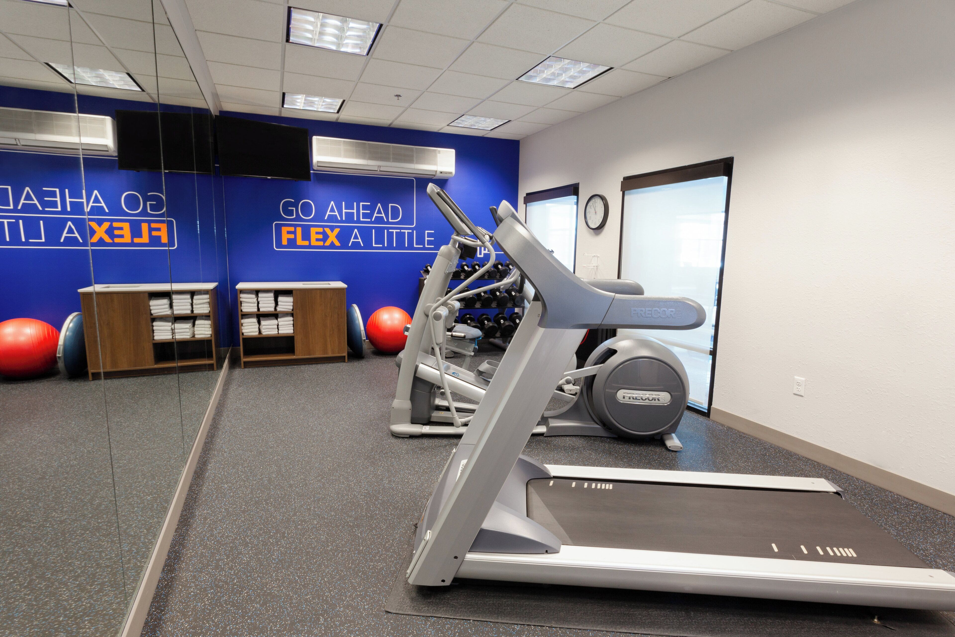 Een sportschool met loopbanden, fitnessballen en een muur met motiverende tekst.