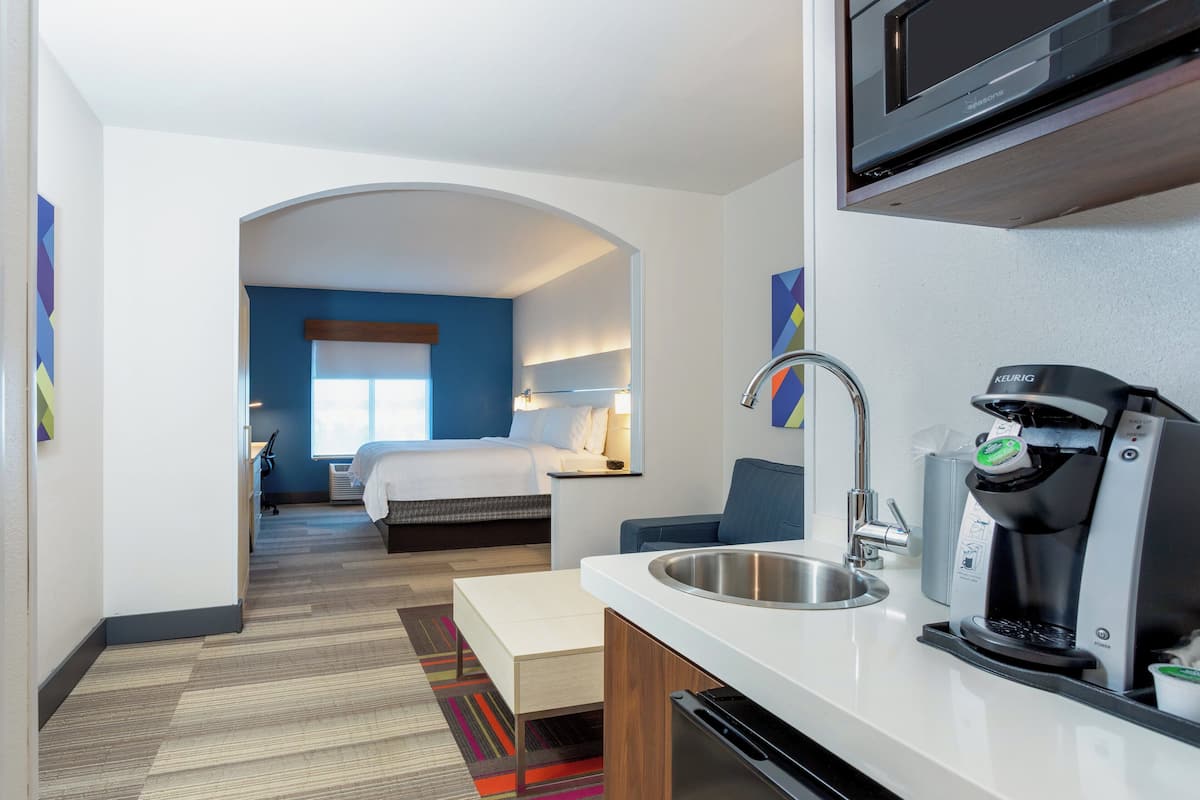 A hotel room with a kitchenette, a bed, a desk, and a view of the hallway.