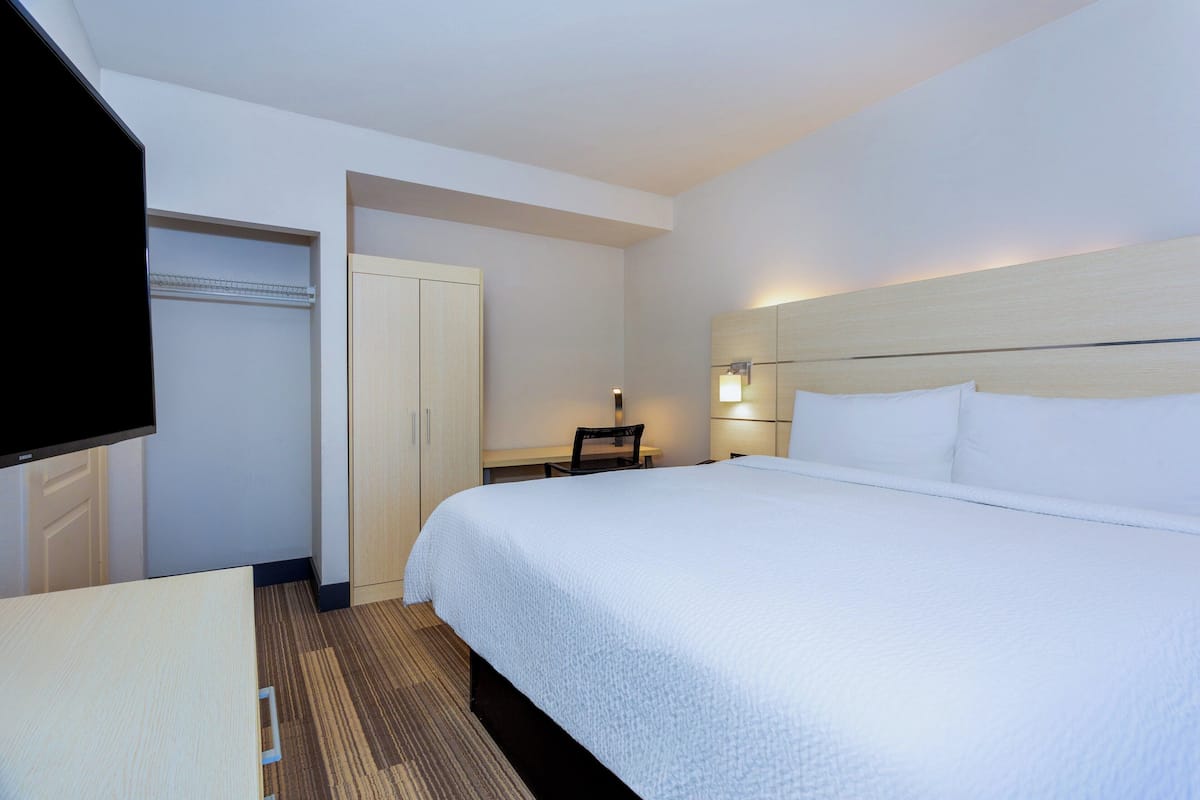 A hotel room with a large bed, a desk, a chair, a TV, and a wardrobe.