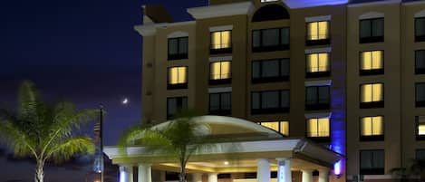 A Holiday Inn Express & Suites hotel with a prominent sign, multiple balconies, and a well-lit entrance.