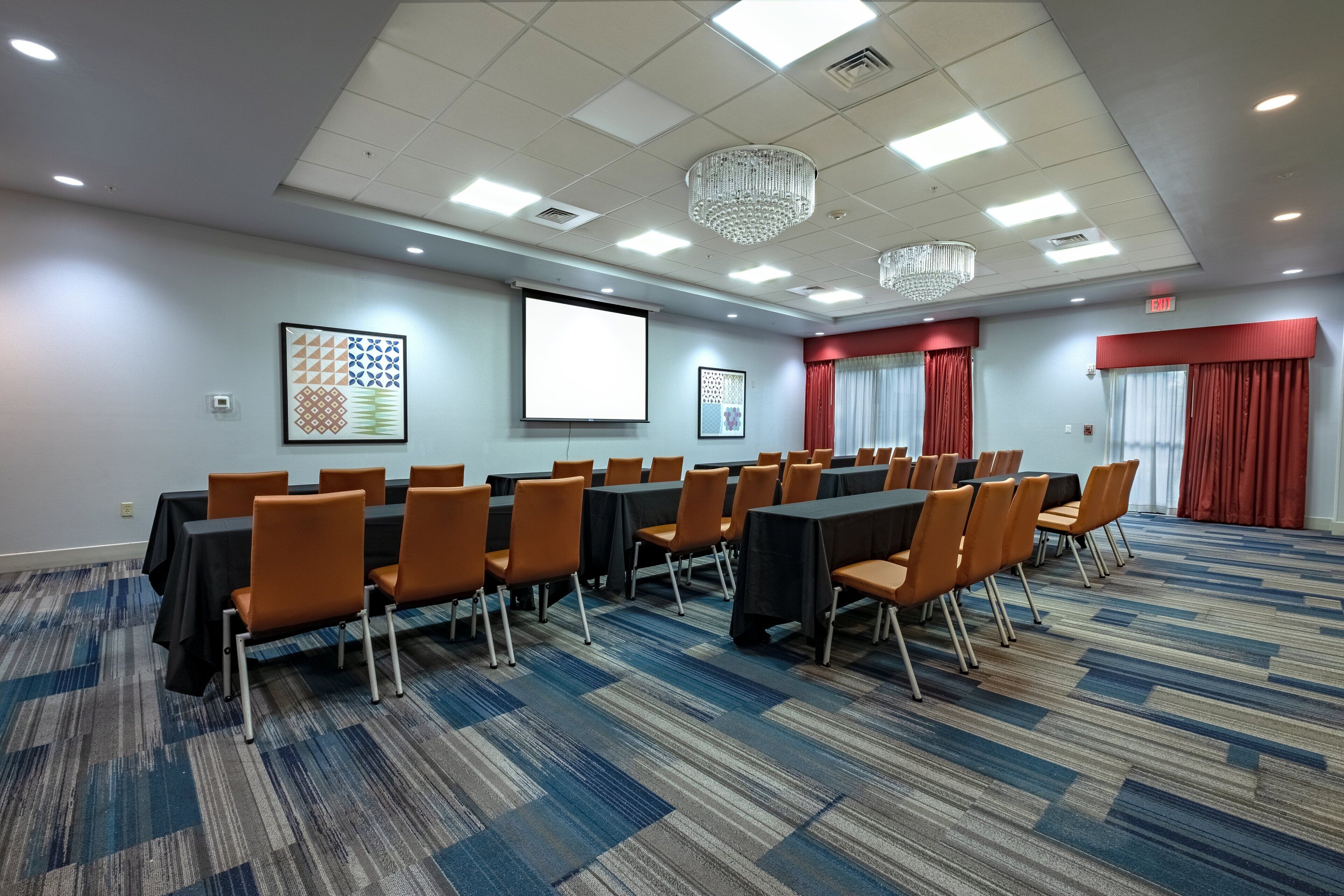 A conference room with tables and chairs, a projector screen, and a carpeted floor.
