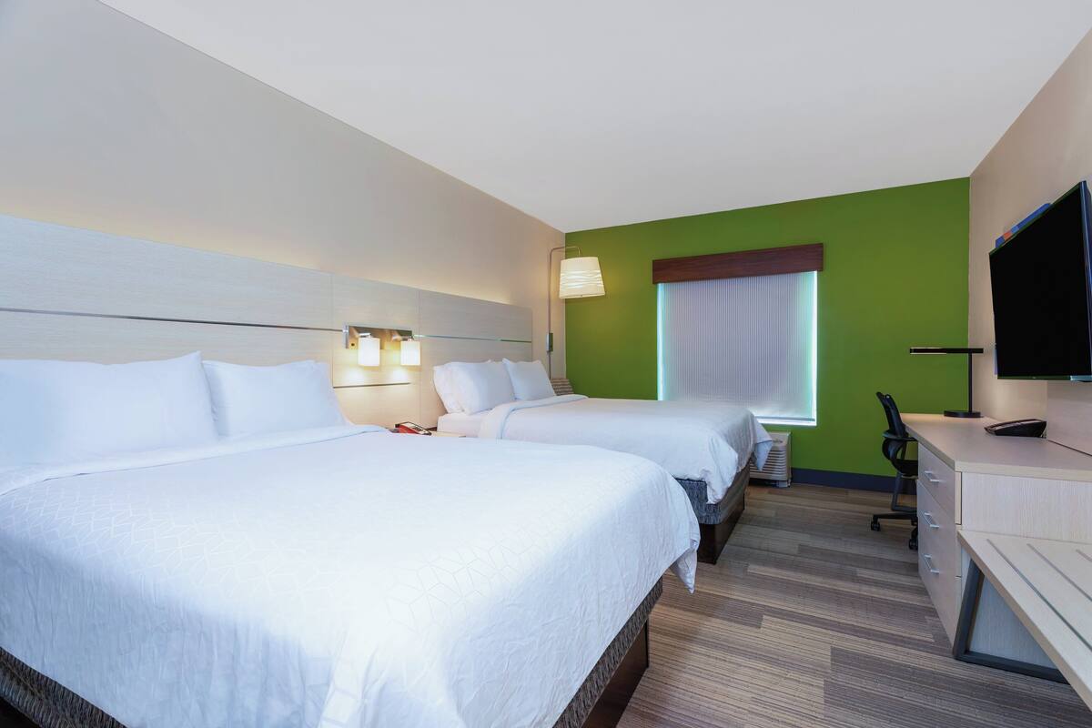 A hotel room with two beds, a desk with a chair, a television, and a window with curtains.