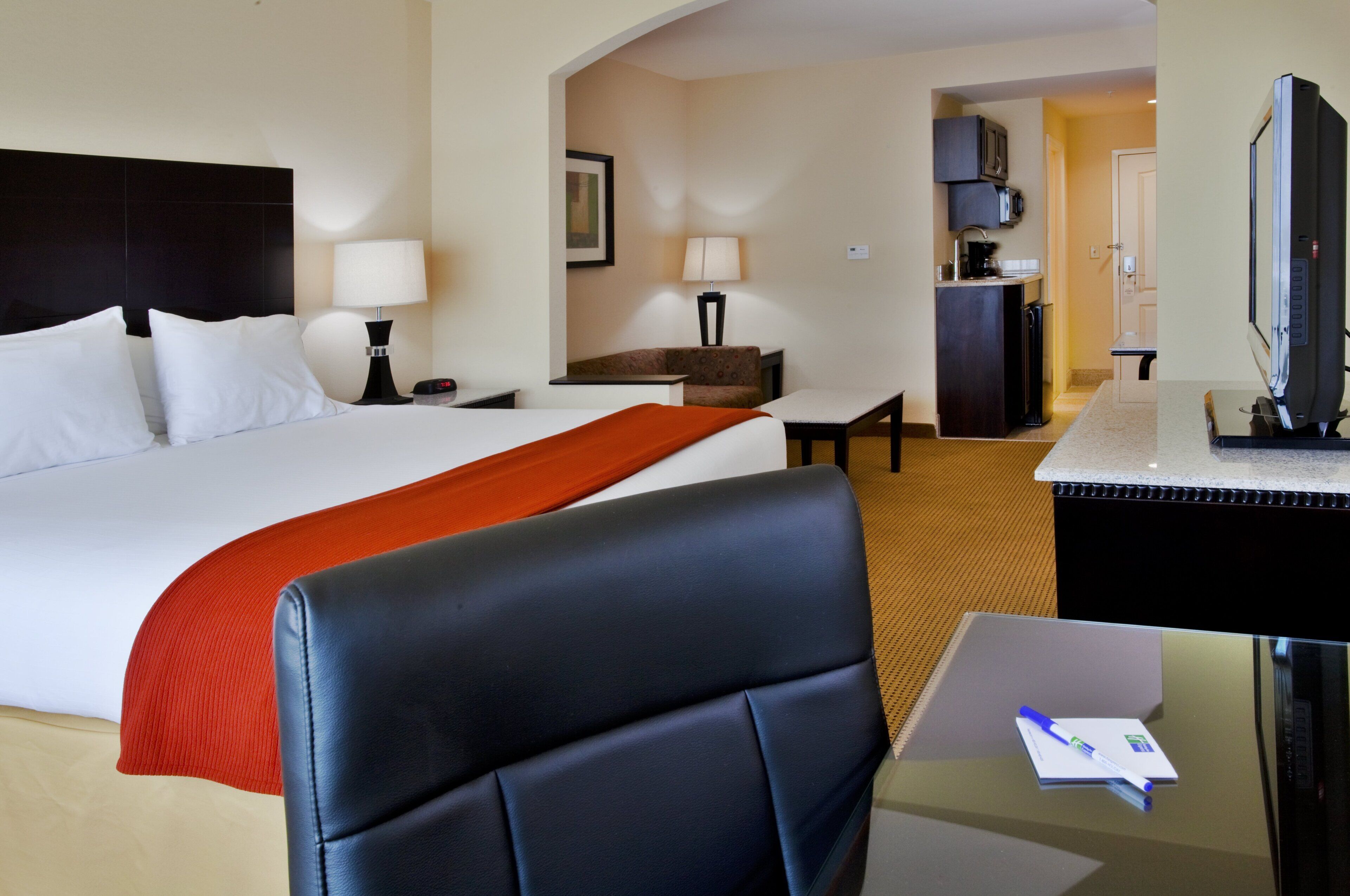 Ein Hotelzimmer mit Bett, Schreibtisch, Stuhl, Fernseher und einer Küchenzeile.