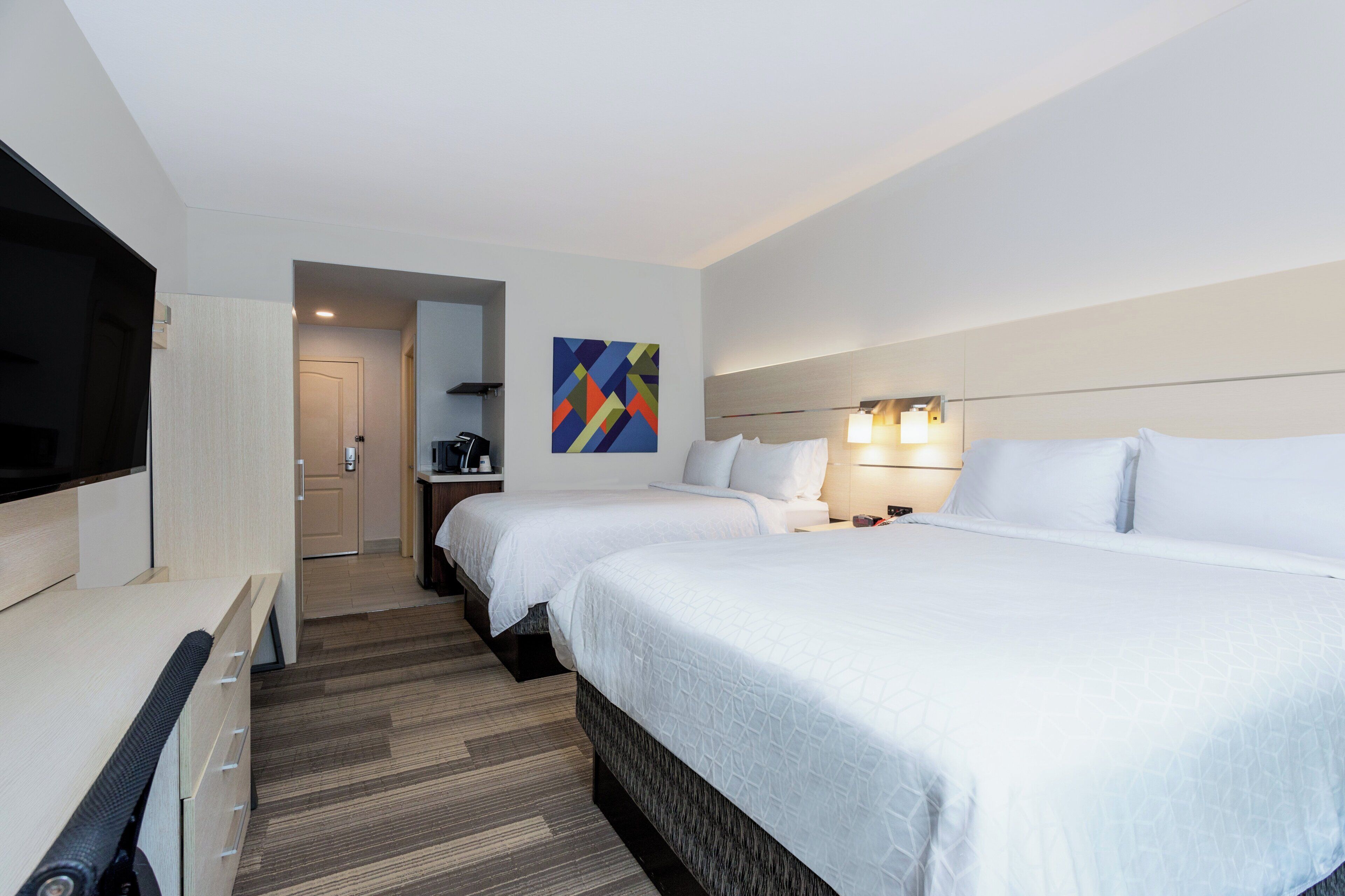 Una habitación de hotel con dos camas, televisión, un cuadro y un escritorio.