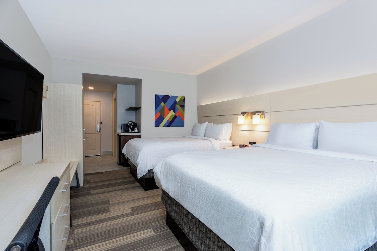 A hotel room with two beds, a TV, a painting, and a desk.