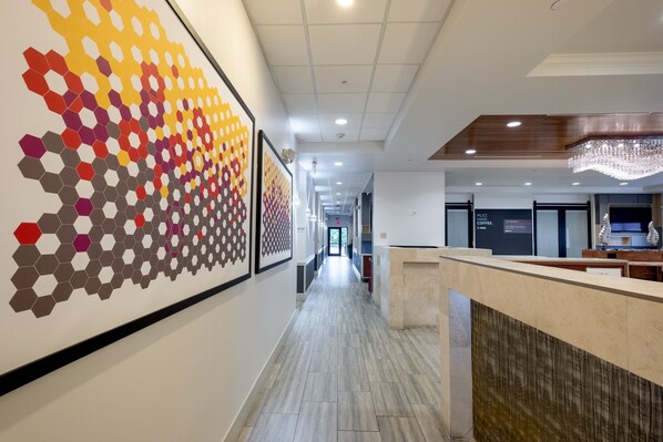 A hotel lobby with a long hallway, a reception desk, and a large wall art installation. - Holiday Inn Express & Suites, International Drive by IHG (Orlando)