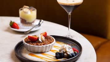 A dessert plate with a bowl of fruit crumble, a scoop of ice cream, and a martini glass with a dark-colored drink.