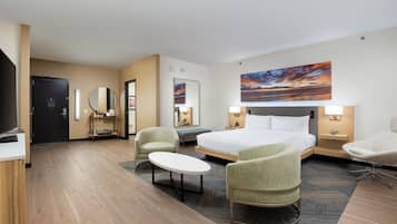A hotel room with a large bed, two armchairs, a small table, a TV, and a painting on the wall.