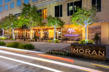 A modern room with a view of a cityscape at night, featuring a blue chair, a round table, and a floor lamp. at The Moran CITYCENTRE